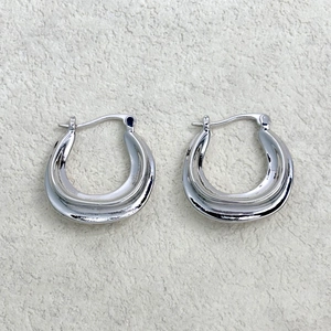 Macro shot of silver-colored chunky U-shaped earrings with polished finish on stone surface