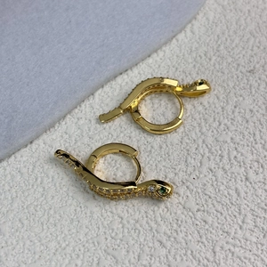 Detailed close-up of gold snake hoop earrings with green eyes and white zircon stones