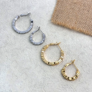 Detail of 18K gold and silver plated square bead earrings on a textured stone surface