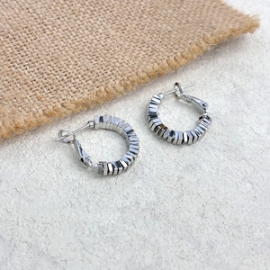 Macro detail of silver geometric beaded C-shape hoop earrings with rectangular segments
