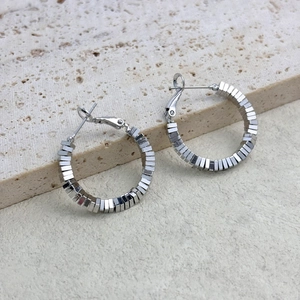 Detailed view of silver hoop earrings featuring geometric square beads on a stone surface