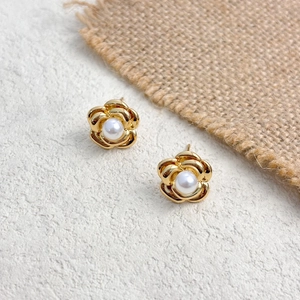 Detailed view of golden camellia earrings with a white pearl on textured background