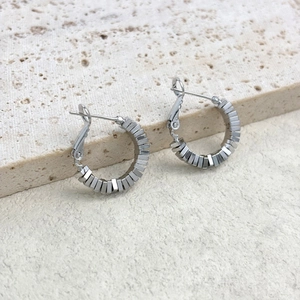 Detail view of geometric cube beaded silver hoop earrings on a textured stone surface