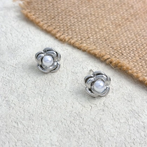 Detailed close-up of small silver flower stud earrings with a pearl center on a textured base