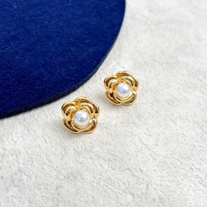Close-up of gold camellia flower earrings with a white pearl center on textured background