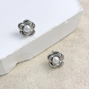 Macro detail of camellia flower stud earrings with central pearl and silver finish