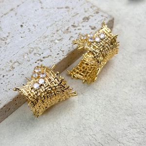 Detailed view of woven hollow gold studs with small sparkling crystals on a stone base