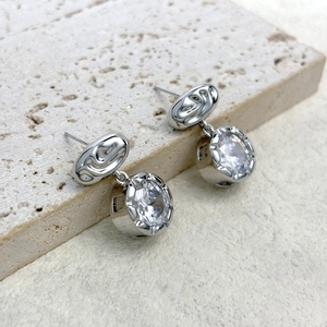 Macro shot of silver fluid-texture earrings with round diamond-cut zircon drops on stone