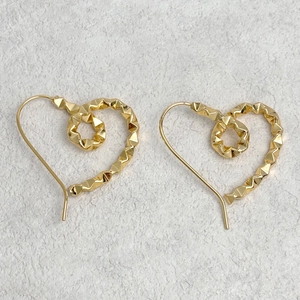 Macro shot of gold hollow heart earrings with geometric texture on stone background