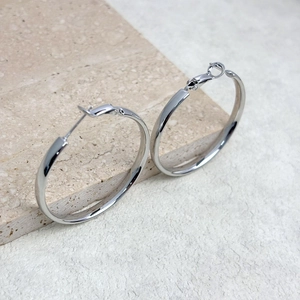 Macro detail of polished large silver hoop earrings on a textured stone surface