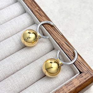 Modern C-shape mixed-tone hoop earrings with a polished gold sphere charm on wood tray