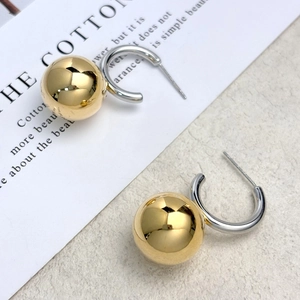 Two-tone sphere drop earrings with 18k gold plated ball and silver hook on a desk