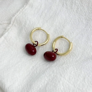 Créoles dorées rétro avec pendentifs ovales rouge foncé sur fond de tissu blanc doux