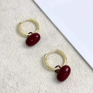 Gros plan de boucles d'oreilles créoles dorées avec pendentifs ovales rouge vin poli