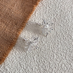 Elegant silver starburst snowflake earrings with sparkling crystals on rustic linen