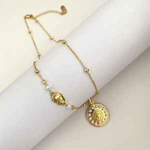 Détail du collier solaire doré avec perle et pendentif relief sur support blanc