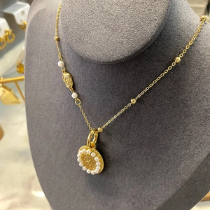 Détail du collier à pendentif pièce dorée avec perles blanches sur un support en velours
