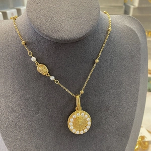 Collier avec pendentif soleil doré et perles blanches sur présentoir gris
