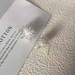 Macro detail of silver snowflake firework stud earring on minimalist textured surface