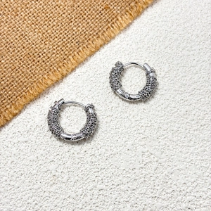 Detailed macro view of French style irregular silver hoop earrings with woven chain texture