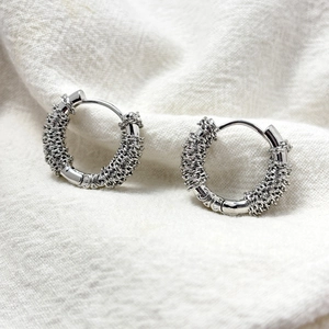 Irregular wire-wrapped silver finish hoop earrings on a natural linen background