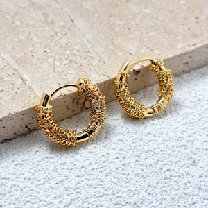 Detailed close-up of gold hoop earrings with intricate wire-wrap texture and hinge clasp