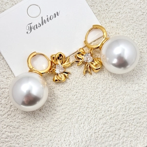 Détail de boucles d'oreilles nœud doré avec cristal cœur et grande perle blanche