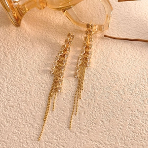 Macro detail of long gold tassel earrings with marquise-cut crystal wheat leaf design