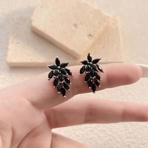Dettaglio macro di orecchini a grappolo in zircone nero su base argento con sfondo in pietra