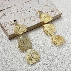 Macro shot of gold-tone tiered petal earrings with clear zircon on beige stone stand
