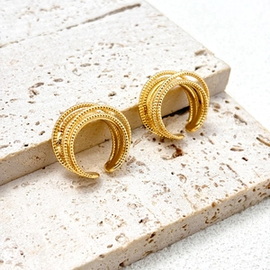 Detailed close-up of gold-plated multi-layer C-shape earrings on light stone