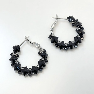 Detailed view of S925 silver hoop earrings with black pyramid-cut zircons on white surface