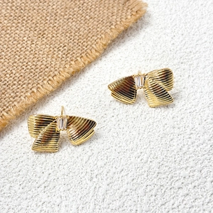 Détail de boucles d'oreilles nœuds dorés avec texture métallique et pierre zircon