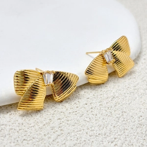 Détail de boucles d'oreilles nœud doré avec texture ondulée et pierre de zircon cubique