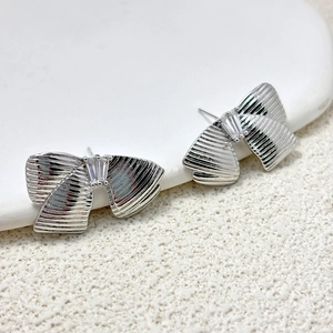 Détail de boucles d'oreilles nœud argentées avec texture brossée et zircon