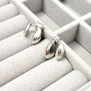 Detail of silver water-drop stud earrings with polished mirror finish on velvet tray