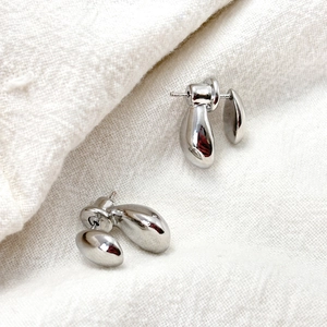 Detailed close-up of organic teardrop liquid metal stud earrings on white linen fabric