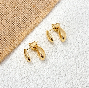 Detail view of gold teardrop earrings with high-polished metallic finish on textured background