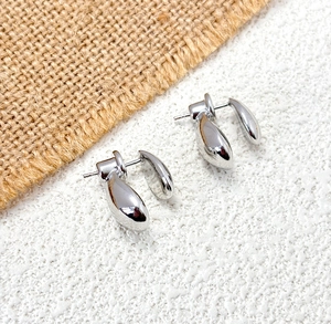 Macro detail of silver teardrop earrings with polished metal finish on textured white surface