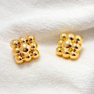 Polished gold beaded cluster stud earrings on white linen fabric background