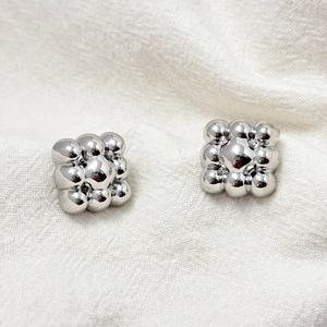Macro shot of silver square earrings composed of stacked metal spheres on white fabric