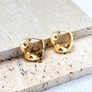 18K gold-plated twisted spiral hoop earrings on a travertine stone display stand