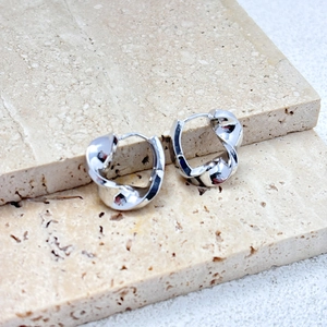 Macro shot of polished silver twisted hoop earrings on minimalist stone slabs