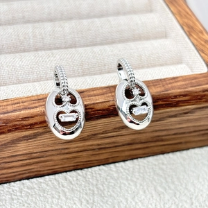 Detail of silver oval earrings with heart cutout and zircon stones on a jewelry box