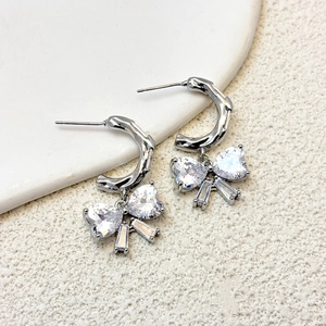 Macro detail of silver bow earrings featuring heart-shaped crystals and C-shaped hoops