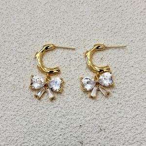 Golden C-shaped hoop earrings featuring a crystal bow pendant with heart-shaped zircons