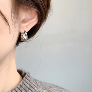 Close-up of polished silver teardrop hoop earrings worn by a model in soft grey tones