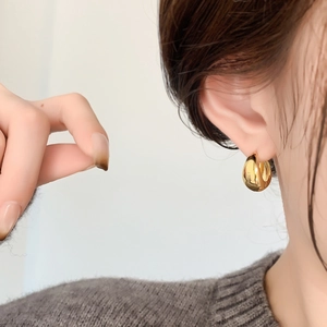 Close-up of a high-polished gold geometric hoop earring worn by a model