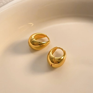 Macro detail of polished gold-plated geometric hoop earrings in a ceramic bowl