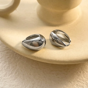 Detailed view of silver organic fluid earrings on a minimalist ceramic display stand